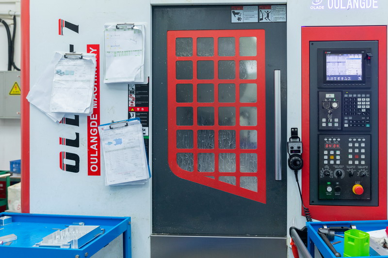 Oulangde CNC machine door with red framed window and printed setup sheets clipped to the panel