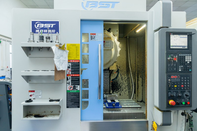 BST CNC machining centre with blue door open showing chip covered tool magazine and vise
