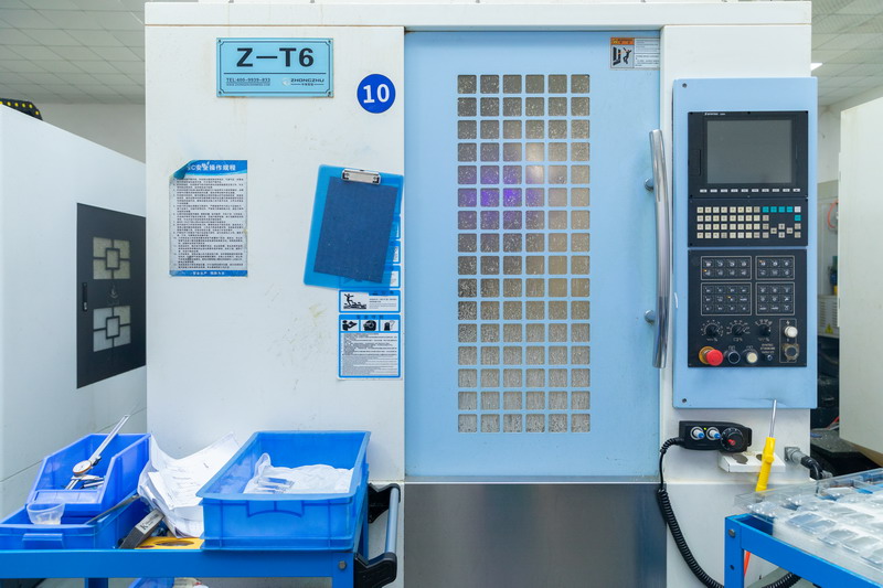 Light blue enclosed vertical CNC machining centre marked Z-T6 with control panel and blue parts bins