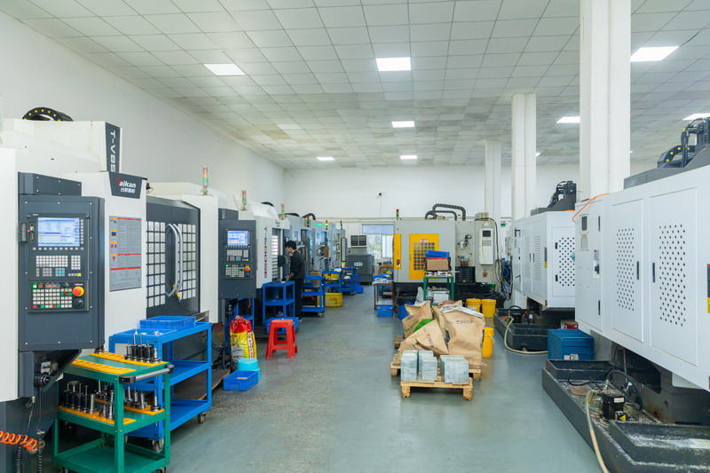 Workshop aisle lined with rows of enclosed CNC machining centres and an operator at work