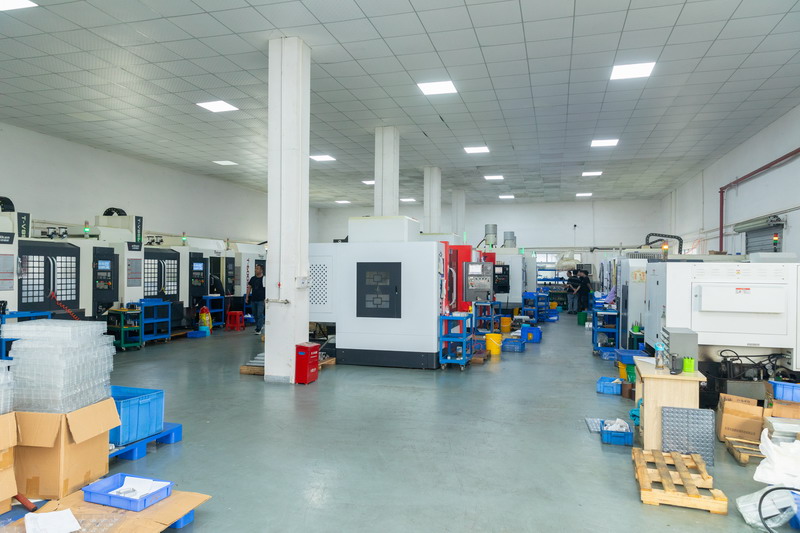 Wide view of a machine shop floor with rows of CNC machining centres and stacked parts bins
